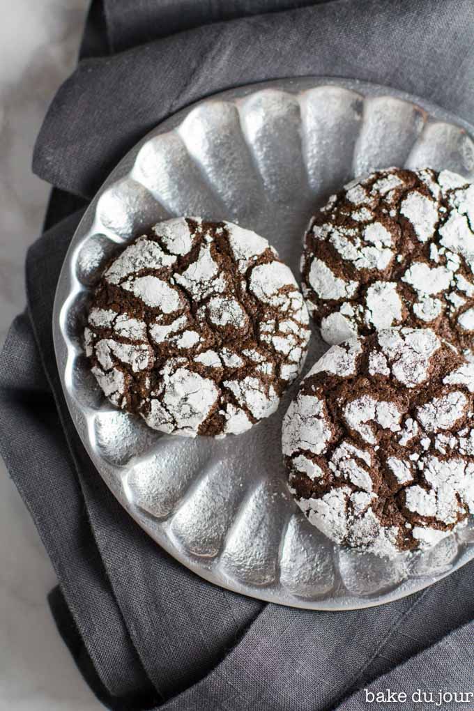 A set of 3 chocolate crinkle cookies on a silver plate