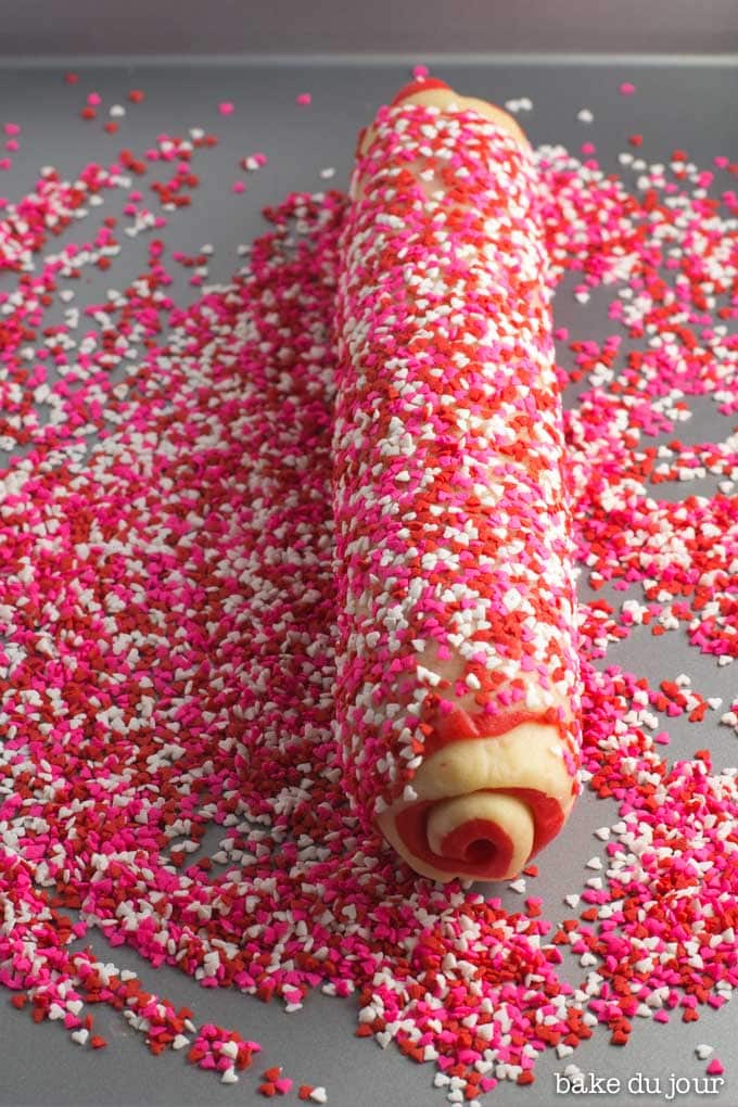 Rolling pinwheel cookie dough log in sprinkles