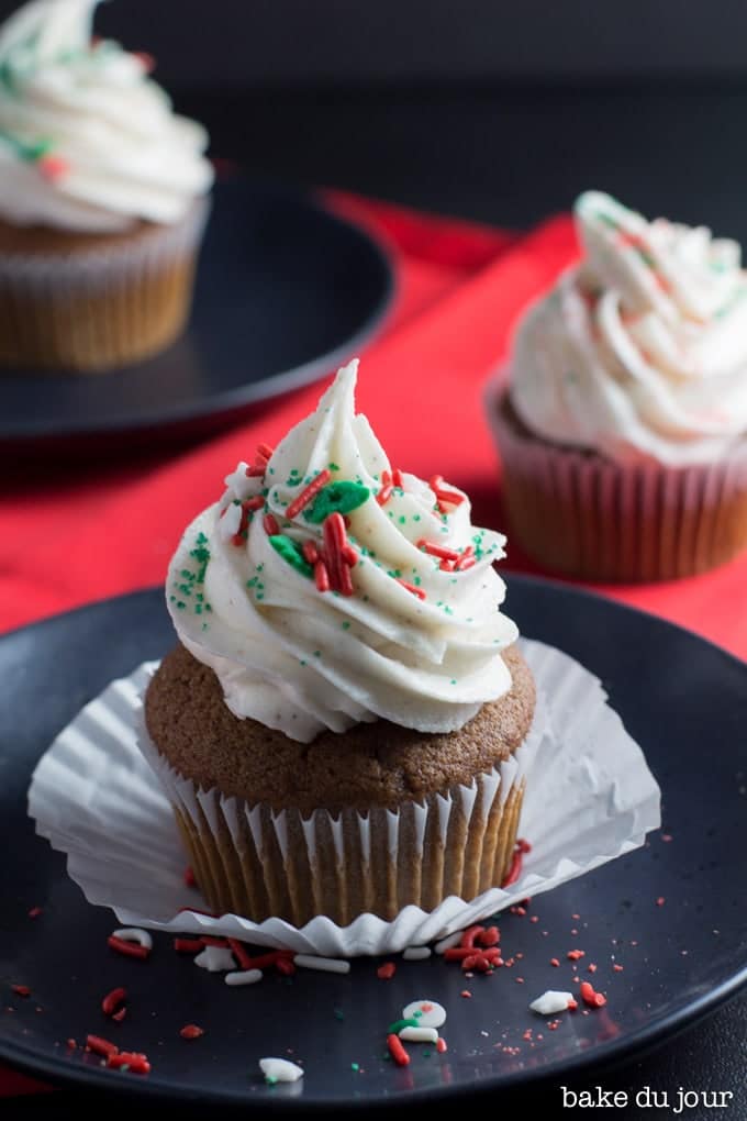 A close up shot of a Gingerbread Eggnog Cupcake on a black dish with a couple of cupcakes in the background