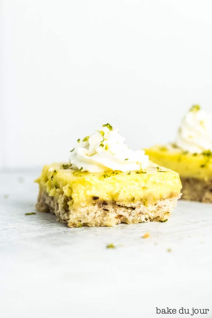 One Coconut Lime Bar topped with whipped cream and lime zest at the forefront, with another bar in the background