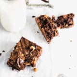 A brownie with a bite taken out of it with a jug of milk in the background