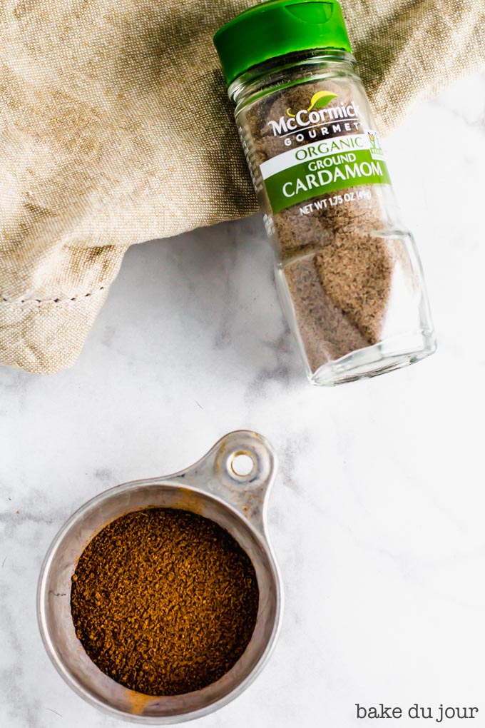 A measuring cup full of spices and a jar of ground cardamom